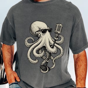 May include: Grey t-shirt with a detailed illustration of an octopus wearing sunglasses and holding a vintage microphone. The octopus is cream-coloured with black accents, and the microphone is silver. The shirt is a solid grey colour.