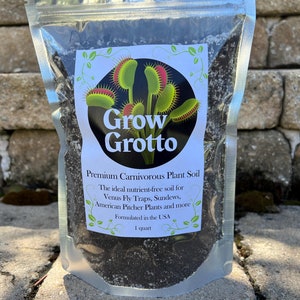 May include: A clear plastic bag filled with dark brown soil. The bag has a white label with the text "Grow Grotto" in black and a graphic of a Venus flytrap. The label also reads "Premium Carnivorous Plant Soil", "The ideal nutrient-free soil for Venus Fly Traps, Sundews, American Pitcher Plants and more", "Formulated in the USA", and "1 quart".