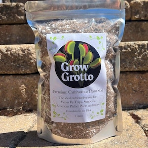 May include: A clear plastic pouch containing 1 quart of brown and white potting mix. The label features a black circle with green and red Venus flytrap illustrations, the text Grow Grotto, and Premium Carnivorous Plant Soil, Formulated in the USA.