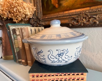 May include: A ceramic casserole dish with a lid, featuring a blue and white checkered pattern on the lid and a blue goose design around the bowl. The dish has two handles and a knob on the lid.