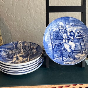 May include: A set of six blue and white ceramic plates with a vintage design. The plates feature illustrations of people in historical clothing. One plate has the word "Farmer" printed on it.