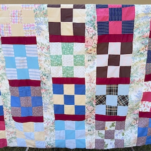May include: A colorful patchwork quilt with a variety of patterns and colors, including squares, stripes, and floral designs. The quilt features a mix of blue, pink, brown, and yellow fabrics, creating a cozy and inviting aesthetic. A handmade textile.
