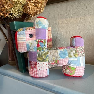 May include: A patchwork fabric dog toy with a red, pink, blue, purple, and green color scheme. The toy is made of different pieces of fabric sewn together to create a unique and colorful design.