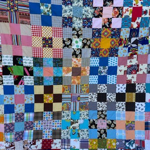 May include: A patchwork quilt with a vibrant mix of fabrics in various colors and patterns. Squares of blue, pink, red, and yellow are arranged in a grid, creating a visually dynamic textile. The quilt showcases a handmade aesthetic.