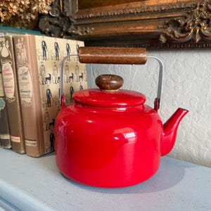 May include: A white ceramic mug with a black handle and the text "But First, Coffee" in a bold, black font. The mug is set against a blurred background, suggesting a cozy setting.