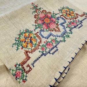 May include: A white linen tea towel with a blue, green, red and yellow embroidered floral design.