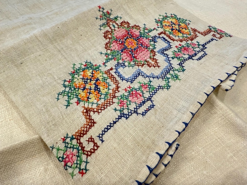 May include: A white linen tea towel with a blue, green, red and yellow embroidered floral design.