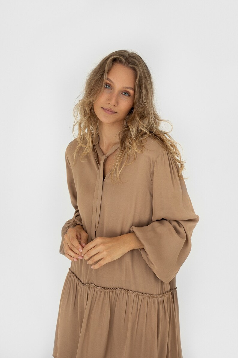 Sandstone loose silhouette dress with tie neckline. Dress has a dropped shoulder line, balloon sleeves anda ruffle at the bottom. image 1