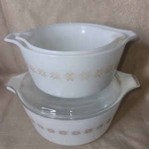 May include: A set of two white Pyrex baking dishes with a gold snowflake pattern. The smaller dish is nested inside the larger dish.