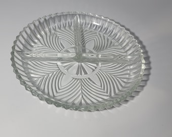 Può includere: Un piatto da portata in vetro trasparente diviso con un bordo smerlato e un motivo geometrico decorativo. Il piatto ha quattro sezioni.