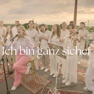 Könnte beinhalten: Eine Gruppe von Menschen singt und spielt Musik auf einem Dach. Die Gruppe trägt weiße Kleidung und die Person vorne trägt eine rosa Hose. Der Text "Ich bin ganz sicher" ist im Bild zu sehen.