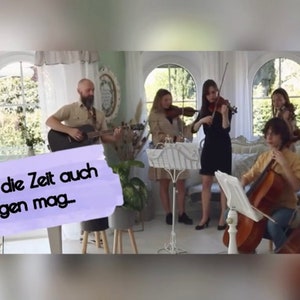 Könnte beinhalten: Eine Gruppe von Musikern spielt Instrumente in einem Raum mit großen Fenstern. Ein Gitarrist spielt eine braune Akustikgitarre, während ein Cellist und drei Violinisten ihre Instrumente spielen. Der Text "Was mir die Zeit auch bringen mag" ist im Bild sichtbar.