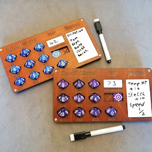 Peut inclure: Deux feuilles de personnage en bois pour jeux de rôle sur table. La feuille du haut a des dés bleus et une section pour des notes avec le texte "Initiative, Tom, PNJ, Kate, 13055, Sarah". La feuille du bas a des dés violets et une section pour des notes avec le texte "PV temporaires +14, Furtivité +10, Vitesse 1/2".