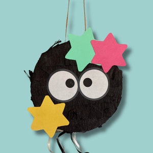 May include: Black pinata shaped like a cartoon character with large eyes and a mouth. The pinata is decorated with three paper stars in pink, green, and yellow.