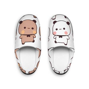 Peut inclure: Une paire de pantoufles d'intérieur blanches avec un motif mignon de panda et d'ours en dessin animé. Les pantoufles ont un fond blanc avec des ours bruns et noirs et des pandas blancs avec des yeux noirs et un nœud papillon noir.