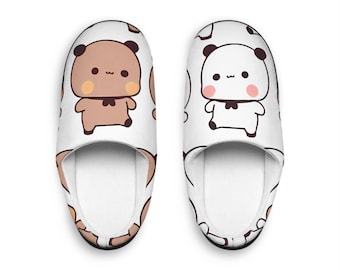May include: A pair of white indoor slippers with a cute cartoon panda and bear design. The slippers have a white background with brown and black bears and white pandas with black eyes and a black bow tie.