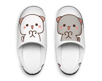 May include: A pair of white indoor slippers with a cute cartoon cat design. One slipper features a white cat with pink cheeks and the other features a gray cat with pink cheeks.