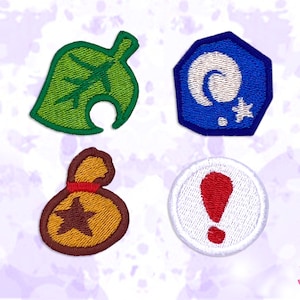 Op de afbeelding: Vier geborduurde patches met ontwerpen uit een videogame. Inclusief een groen blad, een blauw en wit fossiel, een bruine geldbuidel en een witte cirkel met een rode uitroepteken.