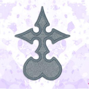 May include: A grey embroidered patch with a symmetrical, ornate design. The patch has a central, elongated shape with a pointed top and rounded base, with curved elements on either side. The design is detailed with textured stitching.