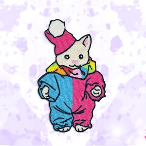 Puede incluir: Parche bordado con un gato de dibujos animados que lleva un gorro rosa con un pompón blanco, una bufanda arcoíris y un mono azul y rosa. El gato tiene la cara blanca y ojos negros. El parche está sobre un fondo lila claro.