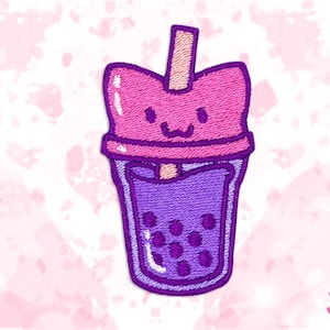 May include: Embroidered patch of a cartoon boba tea drink with a cat-like face. The patch is mainly pink and purple, with a light brown straw. The boba drink has dark purple bubbles.