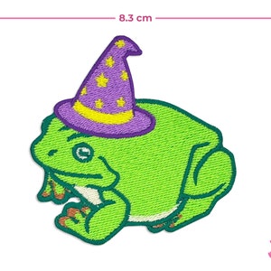 May include: Embroidered patch featuring a green frog wearing a purple wizard hat with yellow stars. The patch measures approximately 3.5 inches wide and 3.5 inches tall. The frog has orange feet and a friendly expression.