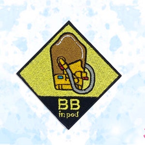 Könnte beinhalten: Gestickter Aufnäher mit gelber Raute, mit einer braunen kapselartigen Form und einer gelben Figur mit einem Schlauch. Der Text "BB in pod" steht unten. Der Aufnäher hat einen schwarzen Rand.