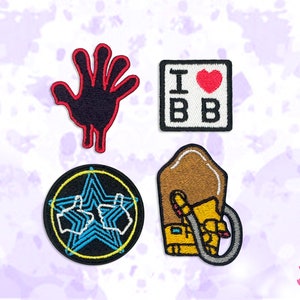 May include: Four embroidered patches with various designs. One shows a black hand with a red outline. Another has "I ❤️ BB" in a square. A third patch has a star with thumbs up. The last patch is a brown and yellow design.