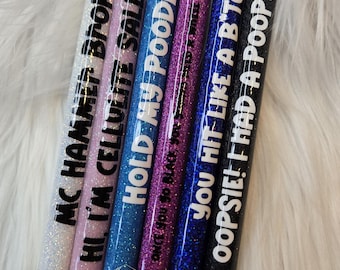 May include: Six glitter pens with black ink and white text. The pens are in different colors: white, pink, blue, purple, dark blue, and black. The text on the pens reads: "MC Hammer Broke", "Hi I'm Cellulite Sally", "Hold My Poodle", "Once You So Black You Hit Like A B*tch", "Oopsie! I Had A Poopsie!"