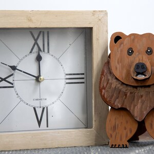 Wooden brown grizzley bear. Brown body & head, darker steaks for fur, Darker brown chest & light streaks for texture. protruding nose to hold glasses, black smaller nose & mouth, black eyes white pupils. sitting on a desk by large clock for size.
