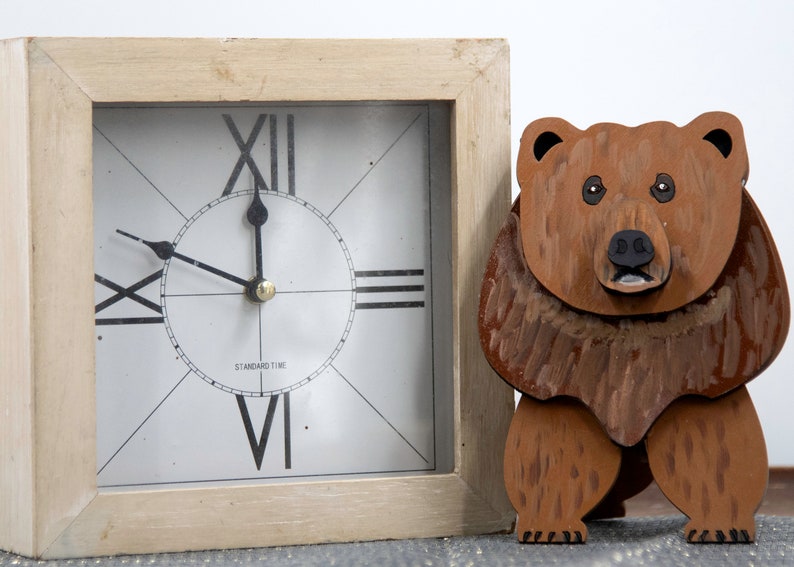 Wooden brown grizzley bear. Brown body & head, darker steaks for fur, Darker brown chest & light streaks for texture. protruding nose to hold glasses, black smaller nose & mouth, black eyes white pupils. sitting on a desk by large clock for size.