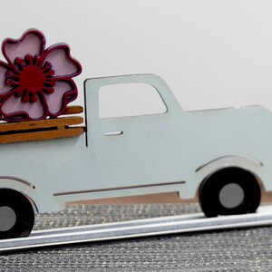 Puede incluir: Una camioneta de madera blanca con una cama de madera marr&oacute;n. Una flor rosa y roja est&aacute; sentada en la cama de la camioneta.