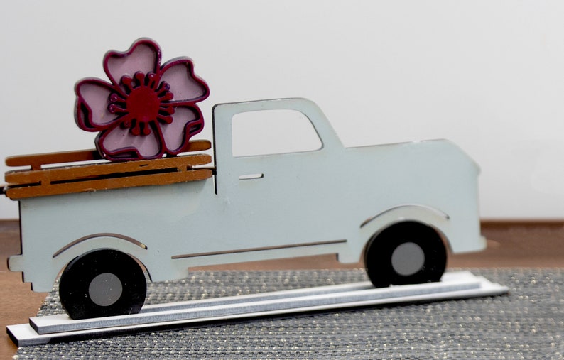 Puede incluir: Una camioneta de madera blanca con una cama de madera marr&oacute;n. Una flor rosa y roja est&aacute; sentada en la cama de la camioneta.