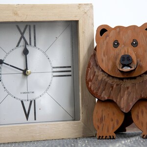 Wooden brown grizzley bear. Brown body & head, darker steaks for fur, Darker brown chest & light streaks for texture. protruding nose to hold glasses, black smaller nose & mouth, black eyes white pupils. sitting on a desk by large clock for size.