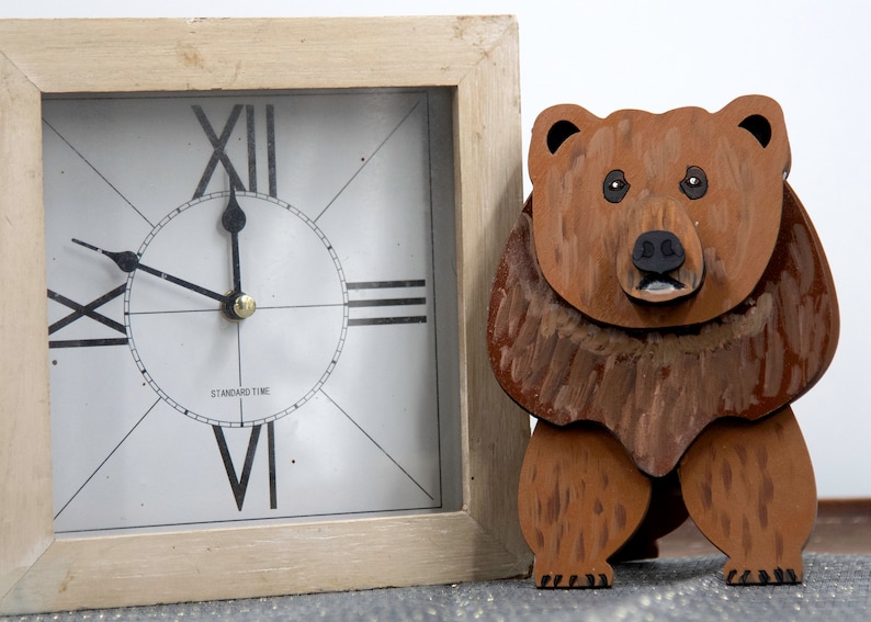 Wooden brown grizzley bear. Brown body & head, darker steaks for fur, Darker brown chest & light streaks for texture. protruding nose to hold glasses, black smaller nose & mouth, black eyes white pupils. sitting on a desk by large clock for size.
