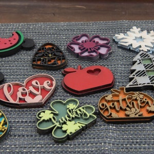 Puede incluir: Una colecci&oacute;n de 12 adornos de madera cortados con l&aacute;ser con varios dise&ntilde;os y colores. Los adornos presentan temas como el amor, la suerte, la reuni&oacute;n, la celebraci&oacute;n, feliz pascua, EE. UU., truco o trato, sand&iacute;a, manzana, copo de nieve y una flor.