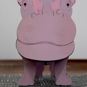 Lavender painted wood standing Hippo figurine. Larger Mouth / nose sticks out to hold glasses. Light pink cute wavy mouth, nostrils, & ears, black eyes white pupils. Cute rounded body and stubby tail. Standing on a desk & silver sparkly placemat