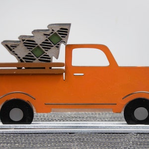 Puede incluir: Cami&oacute;n de madera naranja con un &aacute;rbol de Navidad a cuadros en la caja. El cami&oacute;n est&aacute; sobre una base de madera blanca.