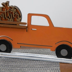 Puede incluir: Cami&oacute;n de madera naranja con una calabaza en la parte trasera que dice "gather" en letras doradas. El cami&oacute;n est&aacute; sobre una base de madera blanca.