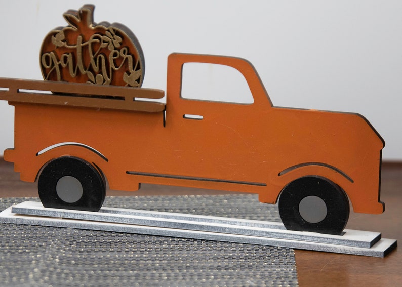 Puede incluir: Cami&oacute;n de madera naranja con una calabaza en la parte trasera que dice "gather" en letras doradas. El cami&oacute;n est&aacute; sobre una base de madera blanca.
