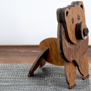 Wooden brown grizzley bear- side view Brown body & head, darker steaks for fur, Darker brown chest & light streaks for texture. Protruding nose holds glasses, black nose & mouth, black eyes white pupils. Side shows light brown body & streaks on desk