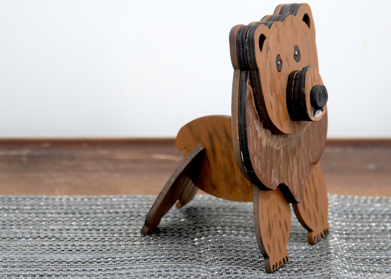 Wooden brown grizzley bear- side view Brown body & head, darker steaks for fur, Darker brown chest & light streaks for texture. Protruding nose holds glasses, black nose & mouth, black eyes white pupils. Side shows light brown body & streaks on desk
