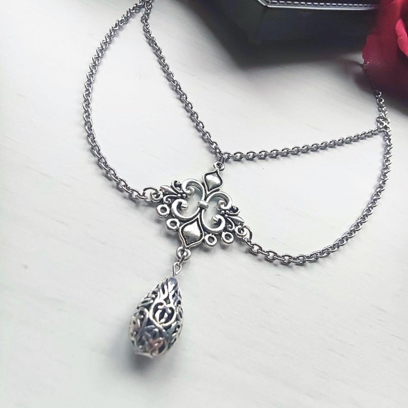 May include: Silver head chain with an elaborate central motif and a hanging teardrop pendant. The headpiece has fine chain links and a detailed filigree design, suitable for special events or themed occasions.
