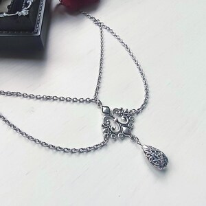 May include: Silver headpiece with an ornate, symmetrical centrepiece and a teardrop-shaped pendant. The headpiece features delicate chain links and an intricate design, suitable for special occasions or themed events.