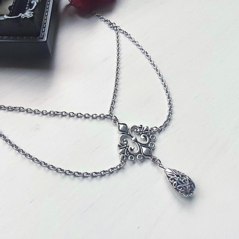 May include: Silver headpiece with an ornate, symmetrical centrepiece and a teardrop-shaped pendant. The headpiece features delicate chain links and an intricate design, suitable for special occasions or themed events.