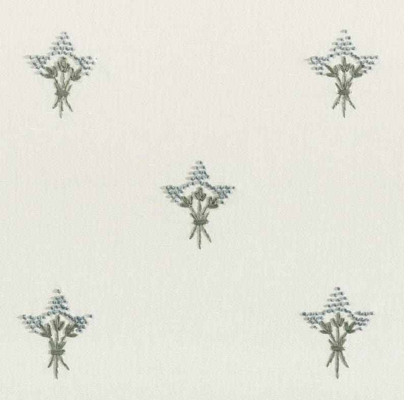 May include: Cream-colored fabric with a repeating pattern of embroidered floral bouquets. Each bouquet features blue-gray flowers and green stems, tied with a green ribbon. The design is evenly spaced across the fabric.