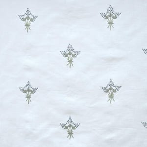 May include: White fabric with a repeating pattern of embroidered floral bouquets. Each bouquet features small, blue-gray flower clusters and green stems, creating a delicate and textured design.