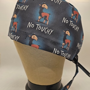 May include: A dark blue scrub cap with a repeating pattern of a cartoon llama and the words "No Touchy" in white. The llama is brown and red. The cap is tied at the back with matching fabric ties.