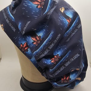 May include: Navy blue scrub cap with a repeating pattern of a cartoon character in a boat, with the text "TODAY IS GOING GREAT, THANKS FOR ASKING." The cap is made of fabric and is designed to cover the head.