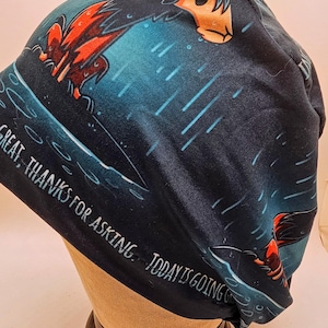 May include: A dark blue beanie with a cartoon dog design in orange, black, and white. The beanie has the text "GREAT, THANKS FOR ASKING. TODAY IS GOING" in white.